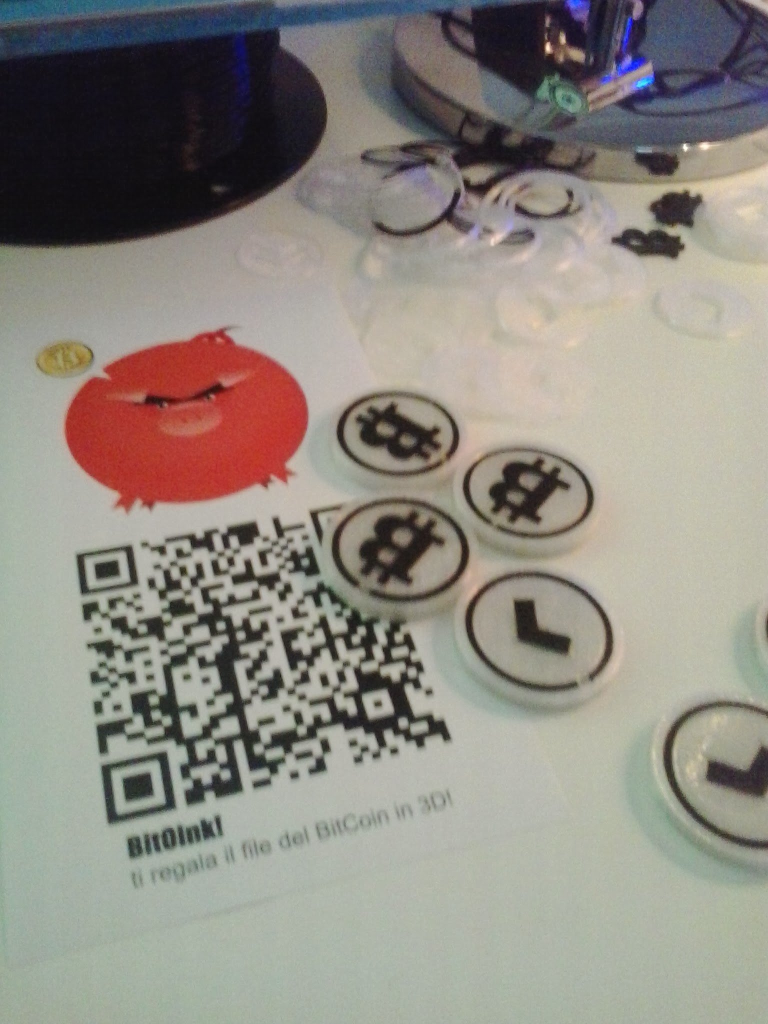Token con il simbolo del Bitcoin stampati in 3D accanto al volantino BitOink con codice QR, Spazio Login Milano, gennaio 2014